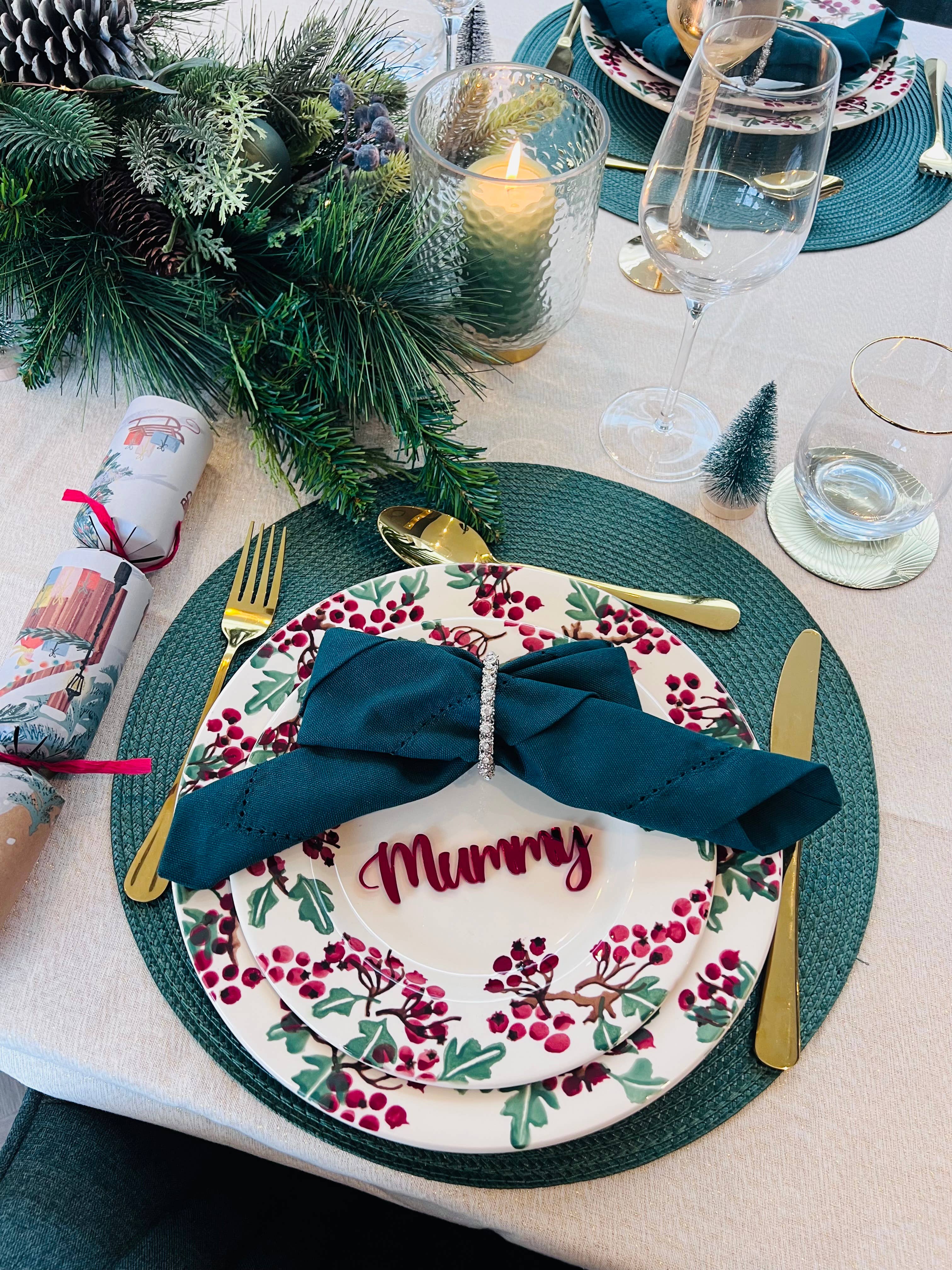 Christmas dinner table setting with personalised acrylic place name ‘Mummy’ in red, festive plate and green napkin
